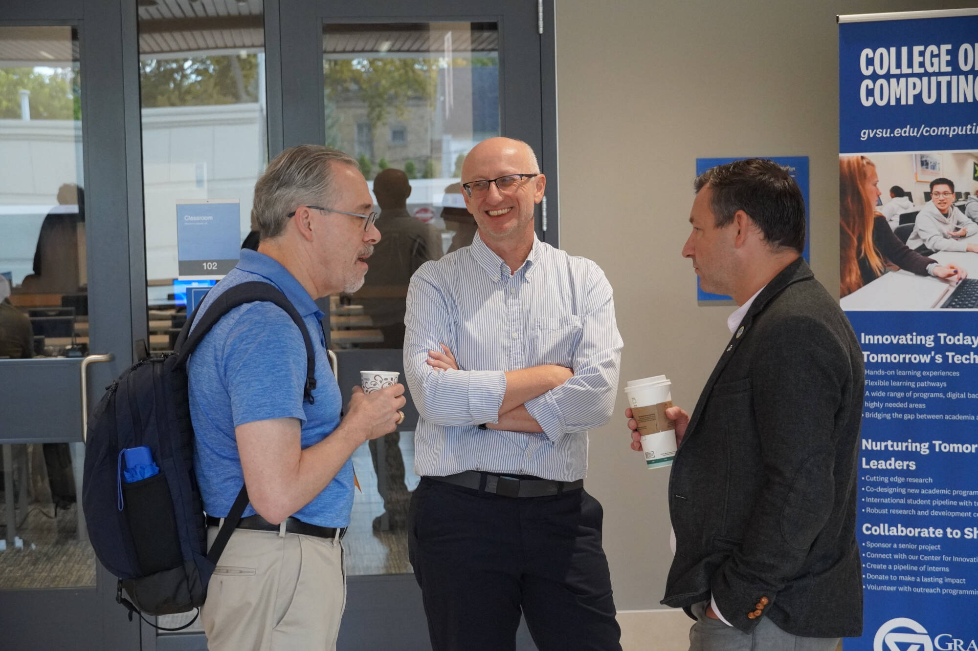 Three Speakers engage in conversation near the College of Computing Conference room entrance.